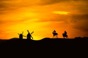Don Quijote y Sancho Panza cabalgan hacia los molinos de viento.