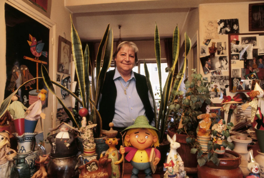 La escritora Gloria Fuertes posa en el interior de su casa, entre macetas y muñecos