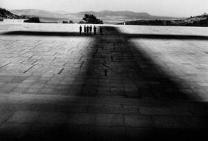 Fotografía que muestra seis figuras bajo la sombra de la cruz del Valle de los Caídos.
